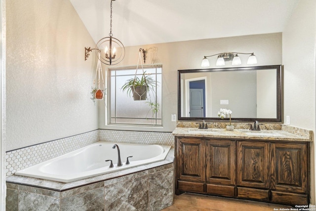 bathroom with a relaxing tiled tub, vanity, vaulted ceiling, and an inviting chandelier