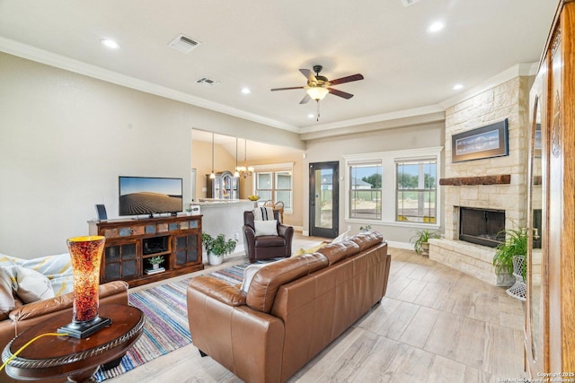 living room featuring crown molding, a stone fireplace, and ceiling fan with notable chandelier