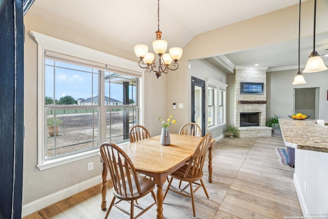 dining area featuring a fireplace, lofted ceiling, a chandelier, ornamental molding, and light hardwood / wood-style flooring