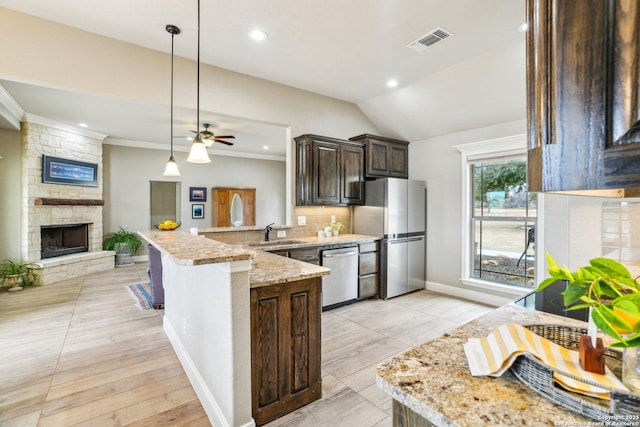 kitchen with appliances with stainless steel finishes, a fireplace, sink, light stone counters, and kitchen peninsula