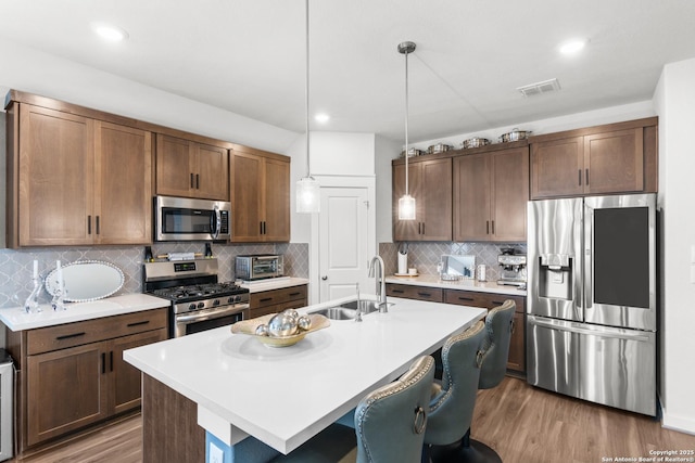 kitchen featuring appliances with stainless steel finishes, decorative light fixtures, sink, and a center island with sink