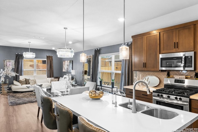 kitchen featuring appliances with stainless steel finishes, sink, decorative backsplash, hanging light fixtures, and light wood-type flooring