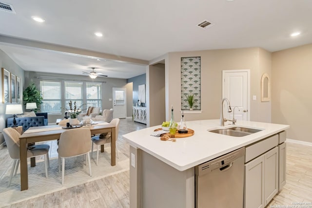 kitchen featuring sink, stainless steel dishwasher, ceiling fan, light hardwood / wood-style floors, and a center island with sink