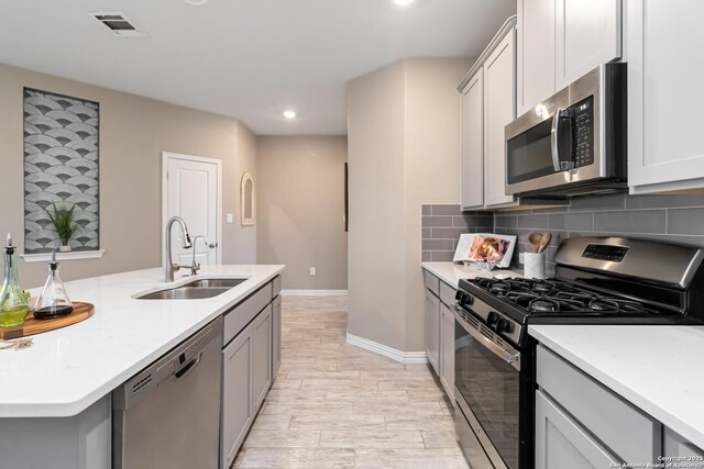 kitchen with gray cabinets, appliances with stainless steel finishes, sink, and backsplash