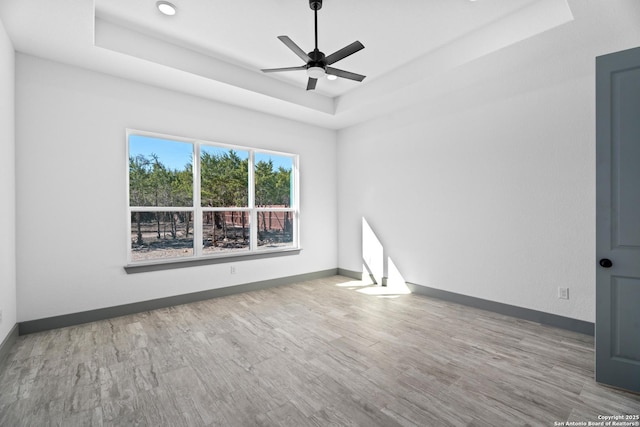 empty room with hardwood / wood-style floors, ceiling fan, and a tray ceiling