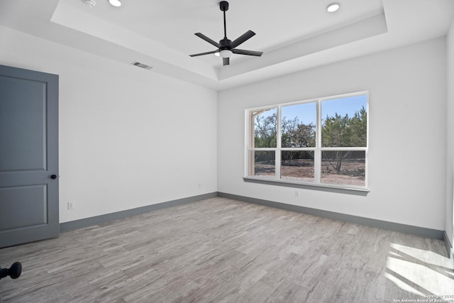 empty room featuring ceiling fan, light wood-type flooring, and a tray ceiling