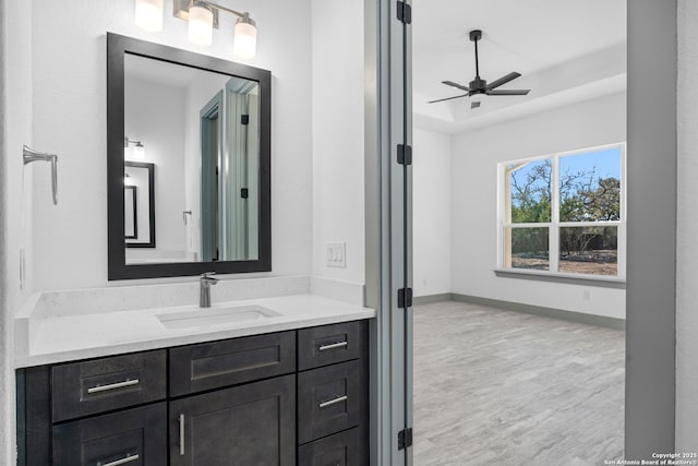 bathroom with vanity, hardwood / wood-style flooring, a raised ceiling, and ceiling fan