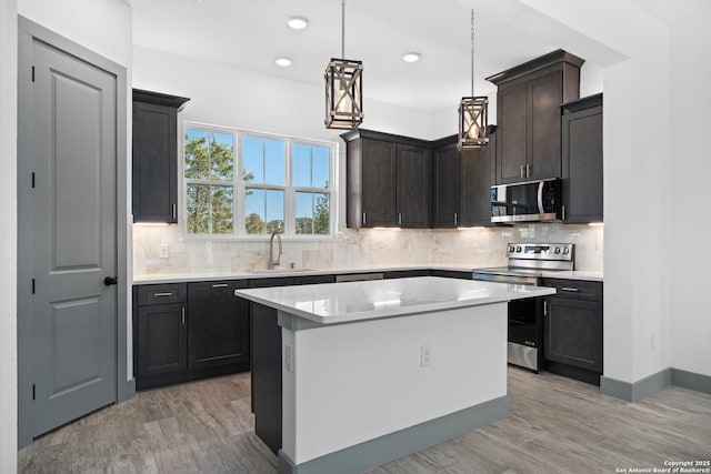 kitchen with sink, hanging light fixtures, appliances with stainless steel finishes, a kitchen island, and decorative backsplash