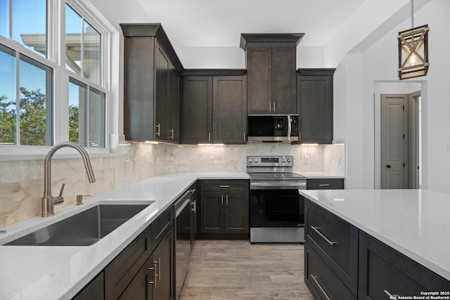 kitchen with sink, light stone counters, decorative light fixtures, appliances with stainless steel finishes, and decorative backsplash