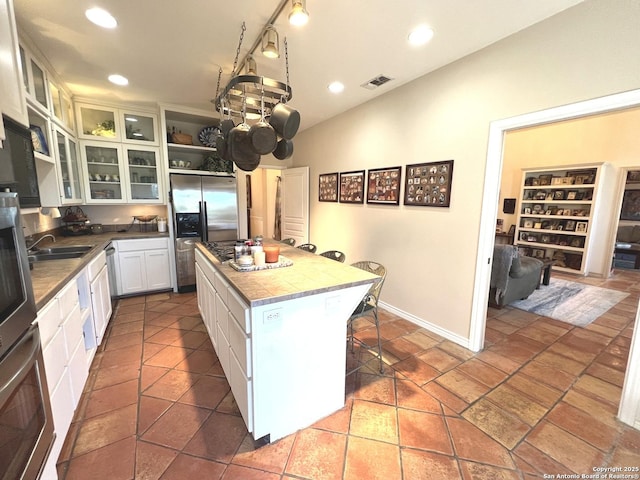 kitchen with sink, appliances with stainless steel finishes, white cabinetry, a center island, and a kitchen bar