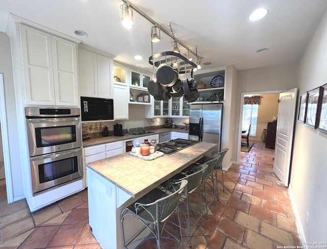 kitchen featuring a kitchen island, white cabinetry, a kitchen breakfast bar, tile counters, and black appliances