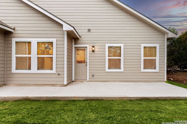 back house at dusk with a lawn and a patio