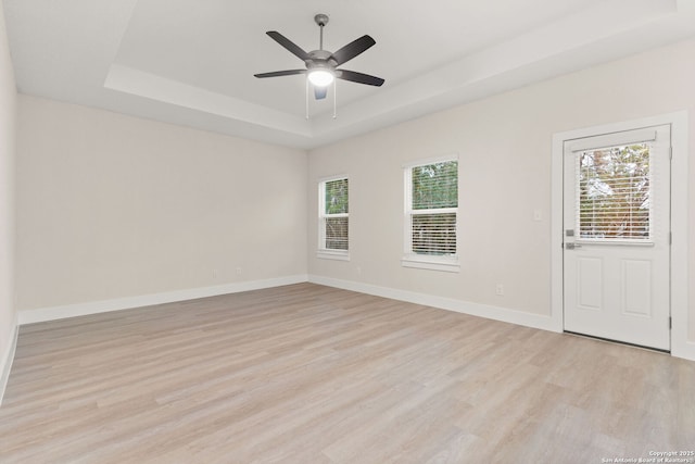 spare room with light hardwood / wood-style flooring, plenty of natural light, a raised ceiling, and ceiling fan