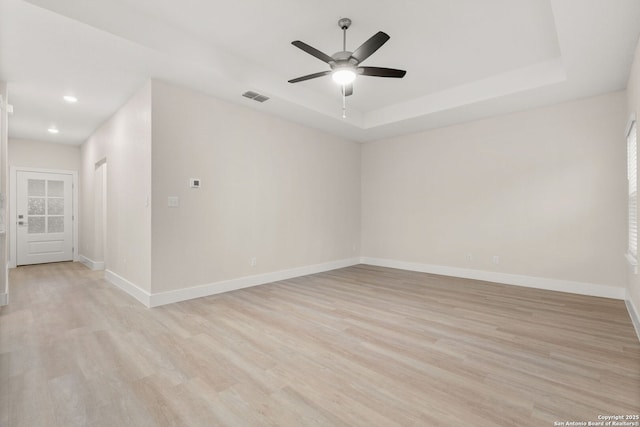 unfurnished room featuring a raised ceiling, ceiling fan, and light wood-type flooring