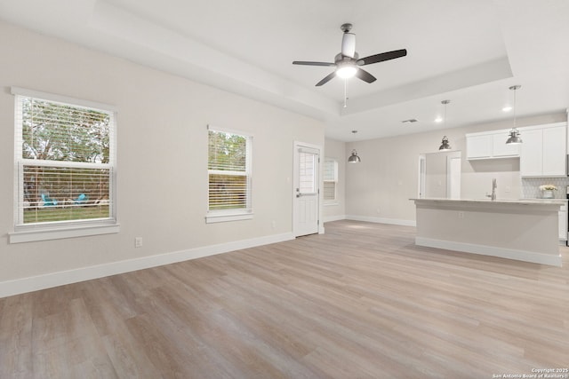 unfurnished living room featuring a raised ceiling, ceiling fan, and light wood-type flooring