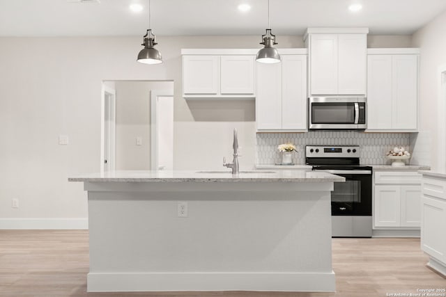 kitchen featuring decorative light fixtures, an island with sink, stainless steel appliances, light stone countertops, and white cabinets