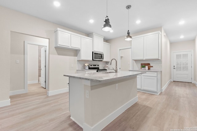 kitchen with sink, hanging light fixtures, stainless steel appliances, a kitchen island with sink, and white cabinets