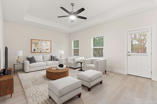 living room featuring ceiling fan, a tray ceiling, light hardwood / wood-style floors, and a wealth of natural light