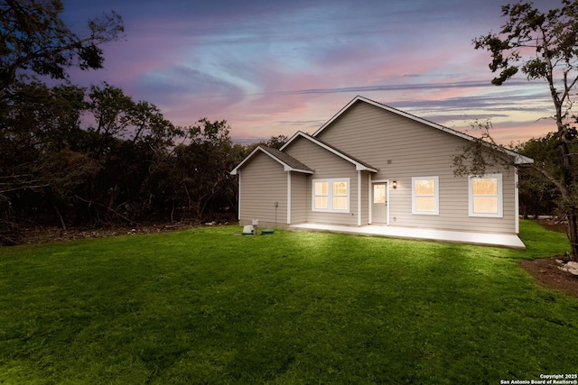 back house at dusk featuring a yard and a patio