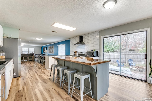 kitchen with a center island, a kitchen breakfast bar, white cabinets, stainless steel appliances, and wall chimney range hood