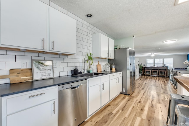 kitchen with sink, appliances with stainless steel finishes, white cabinetry, light hardwood / wood-style floors, and decorative backsplash