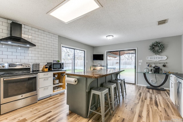 kitchen featuring wall chimney range hood, a breakfast bar area, stainless steel appliances, white cabinets, and a kitchen island