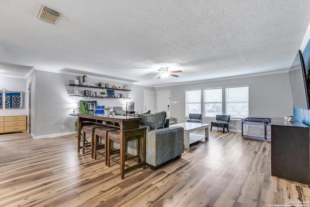 living room featuring a textured ceiling, ornamental molding, light hardwood / wood-style floors, and ceiling fan