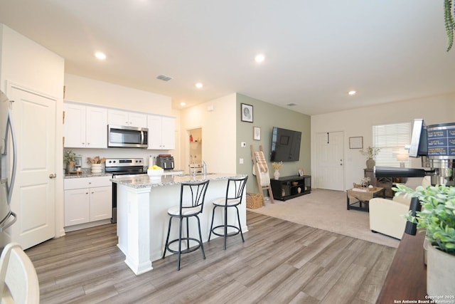 kitchen featuring white cabinetry, a breakfast bar area, a kitchen island with sink, stainless steel appliances, and light stone countertops