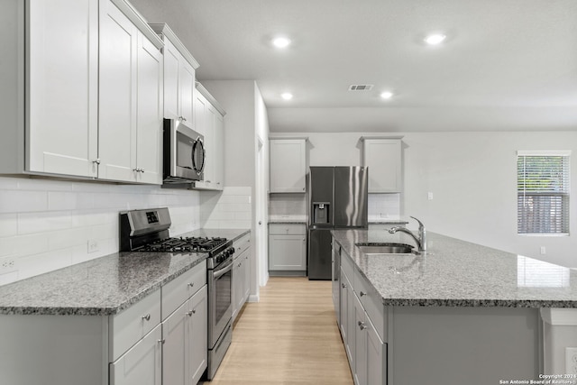 kitchen featuring sink, light hardwood / wood-style floors, stainless steel appliances, light stone countertops, and a center island with sink