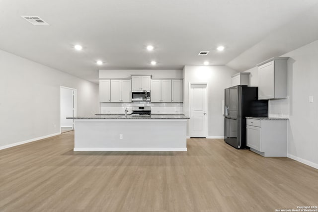 kitchen featuring tasteful backsplash, stainless steel appliances, light hardwood / wood-style floors, and a center island with sink