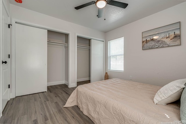 bedroom with hardwood / wood-style floors, multiple closets, and ceiling fan