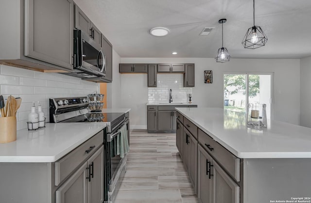 kitchen featuring gray cabinets, a kitchen island, decorative light fixtures, tasteful backsplash, and stainless steel appliances