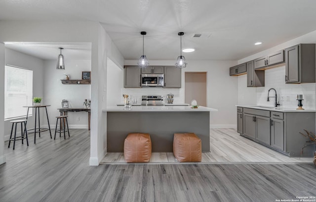 kitchen with stainless steel appliances, sink, gray cabinets, and a breakfast bar area