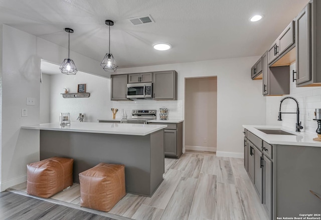 kitchen with sink, appliances with stainless steel finishes, gray cabinetry, decorative light fixtures, and kitchen peninsula