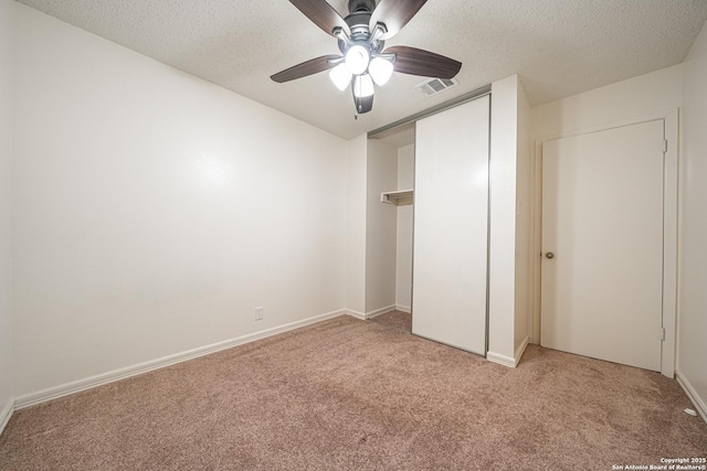 unfurnished bedroom featuring ceiling fan, light carpet, a textured ceiling, and a closet