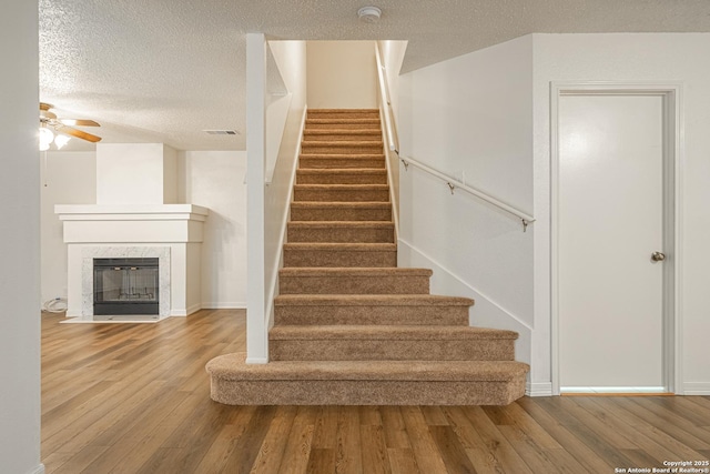 staircase featuring ceiling fan, a high end fireplace, wood-type flooring, and a textured ceiling