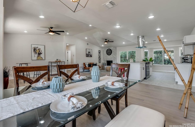 dining area featuring vaulted ceiling, light wood-type flooring, ceiling fan, and a high end fireplace