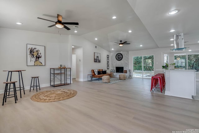 living room with light hardwood / wood-style flooring, a premium fireplace, ceiling fan, and vaulted ceiling