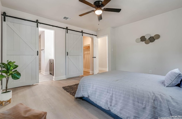 bedroom with ceiling fan, connected bathroom, wood-type flooring, a spacious closet, and a barn door