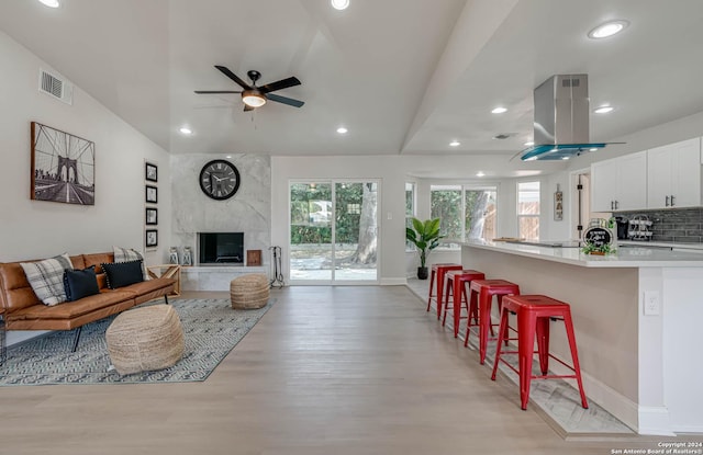 living room with a high end fireplace, light hardwood / wood-style floors, ceiling fan, and plenty of natural light