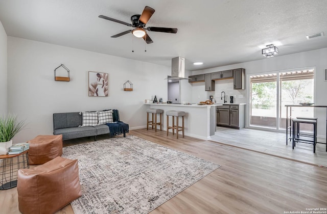 living room featuring sink, light hardwood / wood-style flooring, a textured ceiling, and ceiling fan