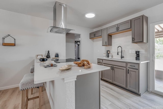 kitchen with sink, a breakfast bar, island range hood, black electric cooktop, and kitchen peninsula