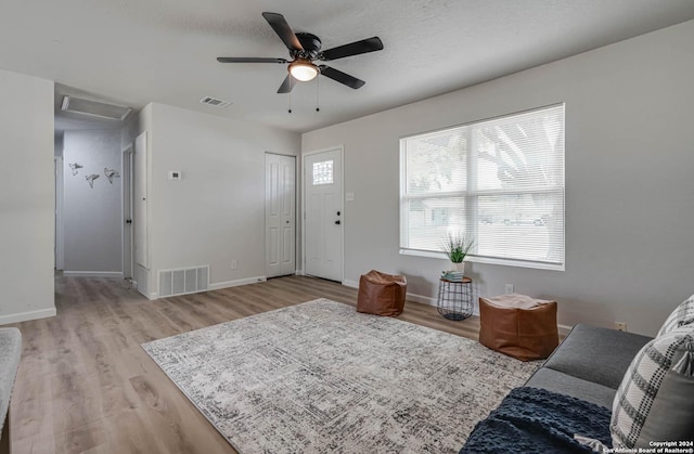 living room with ceiling fan, light hardwood / wood-style flooring, and a textured ceiling