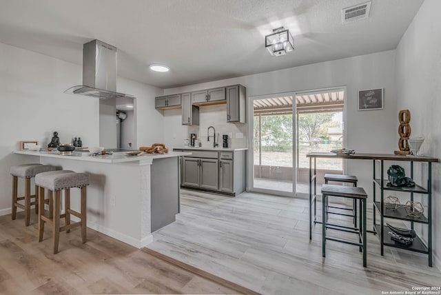 kitchen featuring island exhaust hood, a kitchen breakfast bar, kitchen peninsula, and gray cabinetry