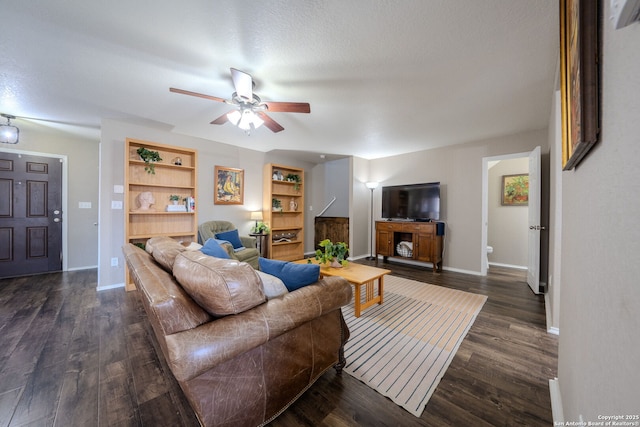 living room with dark wood-type flooring, ceiling fan, built in shelves, and a textured ceiling