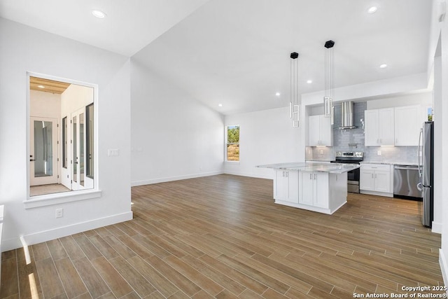 kitchen with decorative light fixtures, a center island, wall chimney range hood, stainless steel appliances, and white cabinets