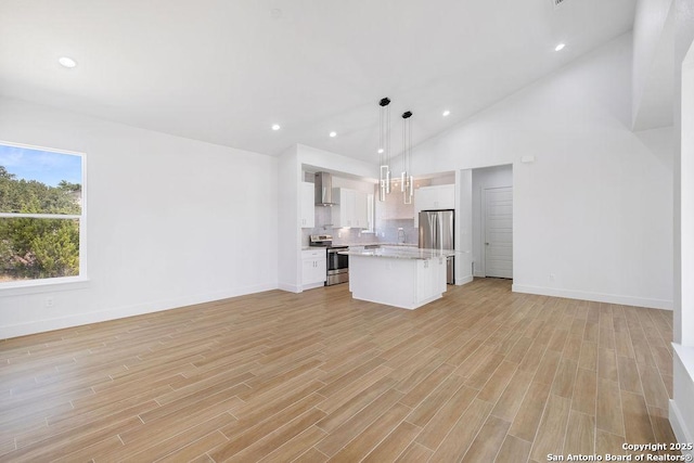 kitchen featuring decorative light fixtures, wall chimney range hood, a kitchen island, stainless steel appliances, and white cabinets