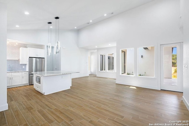 kitchen featuring a kitchen island, stainless steel refrigerator, decorative light fixtures, white cabinetry, and light wood-type flooring