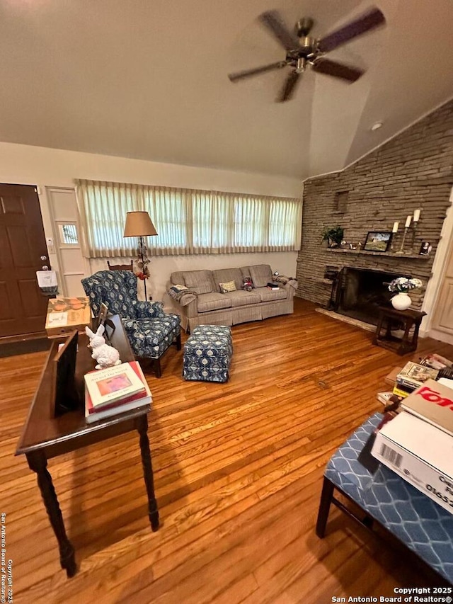 living room with lofted ceiling, a stone fireplace, wood-type flooring, and ceiling fan