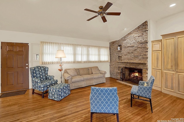 living room featuring ceiling fan, lofted ceiling, a stone fireplace, and light wood-type flooring